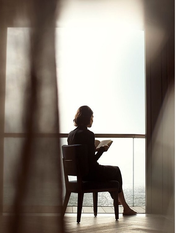 Guest reading by a sunlit balcony with sea view