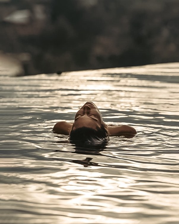 Guest floating in a still infinity pool at golden hour
